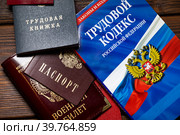 Паспорт, военный билет, трудовая книжка сотрудника и Трудовой кодекс Российской Федерации лежат на столе в отделе кадров предприятия (2023 год). Редакционное фото, фотограф Николай Винокуров / Фотобанк Лори