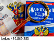 Налоговый кодекс под увеличительным стеклом лежат на столе (2023 год). Редакционное фото, фотограф Николай Винокуров / Фотобанк Лори