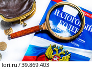 Старый кошелек и Налоговый кодекс под увеличительным стеклом лежат на белом фоне (2023 год). Редакционное фото, фотограф Николай Винокуров / Фотобанк Лори
