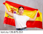 Serious young woman holding state flag of Spain against gray wall background indoors. Стоковое фото, фотограф Яков Филимонов / Фотобанк Лори