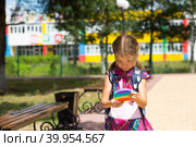 Little girl with a backpack and in a school uniform in the school yard plays pop it toy. Back to school, September 1. The pupil relaxes after lessons. Primary education, elementary class for student. Стоковое фото, фотограф Ольга Симонова / Фотобанк Лори