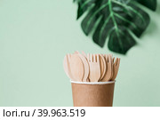 Экологически чистая одноразовая кухонная утварь в бумажном стаканчике на бежево-зеленом фоне. Деревянные вилки, ложки и ножи. Экология, концепция нулевых отходов. Стоковое фото, фотограф Photojuli / Фотобанк Лори