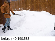 A man in winter cleans snow with a shovel in the yard of a house in the parking lot. Snowfall, difficult weather conditions, the car is stalling, digging up the passage. Стоковое фото, фотограф Ольга Симонова / Фотобанк Лори