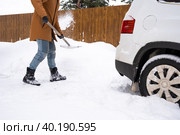 A man in winter cleans snow with a shovel in the yard of a house in the parking lot. Snowfall, difficult weather conditions, the car is stalling, digging up the passage. Стоковое фото, фотограф Ольга Симонова / Фотобанк Лори