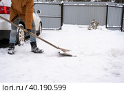 A man in winter cleans snow with a shovel in the yard of a house in the parking lot. Snowfall, difficult weather conditions, the car is stalling, digging up the passage. Стоковое фото, фотограф Ольга Симонова / Фотобанк Лори