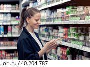 A young smiling lady chooses and buys yogurts in a store. Стоковое фото, фотограф Владимир Разгуляев / Фотобанк Лори
