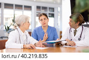 three positive doctors are sitting at table animatedly and actively discussing current work. Стоковое фото, фотограф Яков Филимонов / Фотобанк Лори