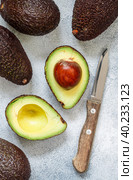 Whole and cut in half ripe organic avocados and a knife on a grey  background. The Haas Avocado. Source of vitamins , trace elements , beta-carotene and omega-3 fatty acids . Healthy food, diet. Стоковое фото, фотограф Виктория Панченко / Фотобанк Лори