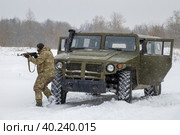Боец в камуфляже с автомтом Калашникова занимает позицию у бронеавтомобиля "Тигр" снежным днем. Военно-исторический парк "Стальной десант", Красное село (2023 год). Редакционное фото, фотограф Виктор Карасев / Фотобанк Лори