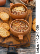 Two servings of traditional French onion soup with baguette and gruyere cheese (emmental, comte or beaufort) in ceramic bowls on a wooden background. Selective focus. Стоковое фото, фотограф Виктория Панченко / Фотобанк Лори
