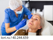 Cosmetologist making injections of botulotoxin in face of mature woman. Стоковое фото, фотограф Яков Филимонов / Фотобанк Лори