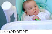 A hungry baby is gnawing on a plastic spoon at the table on a high chair. Teething, whims, itchy gums, introduction of complementary foods. Стоковое видео, видеограф Ольга Симонова / Фотобанк Лори