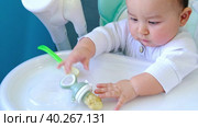 A hungry baby is gnawing on a plastic spoon at the table on a high chair. Teething, whims, itchy gums, introduction of complementary foods. Стоковое видео, видеограф Ольга Симонова / Фотобанк Лори