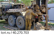 Team of workers with drilling rig on car are drilling artesian well for water in ground. Insertion of metal casing pipe into ground, installation of individual drinking supply, June 28, 2022, Russia, Palaces. Редакционное видео, видеограф Ольга Симонова / Фотобанк Лори