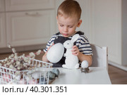 A little boy and a white Easter bunny. We are preparing the family for a Bright Easter. A child is playing with eggs. Стоковое фото, фотограф Photojuli / Фотобанк Лори