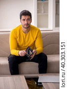 Young man sitting at home in remuneration concept. Стоковое фото, фотограф Elnur / Фотобанк Лори