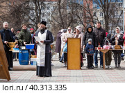 Russia, the City of Vidnoye, April 15, 2023. Easter service. The priest sprinkles people and Easter treats with holy water at the entrance to the temple. People go to sanctify eggs and cakes. Редакционное фото, фотограф Photojuli / Фотобанк Лори
