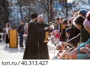 Russia, the City of Vidnoye, April 15, 2023. Easter service. The priest sprinkles people and Easter treats with holy water at the entrance to the temple. People go to sanctify eggs and cakes. Редакционное фото, фотограф Photojuli / Фотобанк Лори