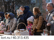Russia, the City of Vidnoye, April 15, 2023. Easter service. The priest sprinkles people and Easter treats with holy water at the entrance to the temple. People go to sanctify eggs and cakes. Редакционное фото, фотограф Photojuli / Фотобанк Лори