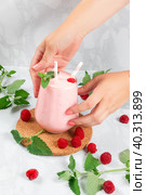 Women's hands put a milkshake with raspberries in a glass glass on the table. Стоковое фото, фотограф Неведицына Елена / Фотобанк Лори