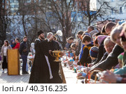 Russia, the City of Vidnoye, April 15, 2023. Easter service. The priest sprinkles people and Easter treats with holy water at the entrance to the temple. People go to sanctify eggs and cakes. Редакционное фото, фотограф Photojuli / Фотобанк Лори