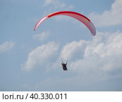 Paraglider with a passenger on a red and white paraglider in a blue sky with clouds. An athlete on a paraglider with a girl. 1st Russian Paragliding Acrobatics Cup Russia Kamyshevatskaya 14.06.2021. Стоковое фото, фотограф Александр Кротков / Фотобанк Лори
