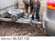 A man checking the hitch mechanism on a car trailer in bad weather. Стоковое фото, фотограф Коханова Наталья / Фотобанк Лори
