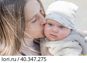 A young mother holds a charming little son in her arms. The kid looks at the camera and smiles. Portrait of a beautiful chubby 4-month-old baby. Стоковое фото, фотограф Photojuli / Фотобанк Лори