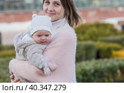 A young mother holds a charming little son in her arms. The kid looks at the camera and smiles. Portrait of a beautiful chubby 4-month-old baby. Стоковое фото, фотограф Photojuli / Фотобанк Лори