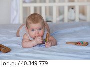 A charming boy in a bright bedroom. A newborn baby is lying on the bed and gnawing on toys. Teeth are teething. The baby's gums are itching. Family, pregnancy and childbirth. Стоковое фото, фотограф Photojuli / Фотобанк Лори