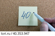 Надпись 40% на бумажном стикере приклеенном к пробковой  доске. Женщина пишет маркером на желтой бумаге. Синий фломастер в женской руке. Рукописный текст красивым почерком. Процент скидки или прибыли. The inscription is 40% on a paper sticker glued to a cork board. A woman writes with a marker on yellow paper. A blue felt-tip pen in a woman's hand. Handwritten text in a beautiful handwriting. Percentage of discount or profit. Стоковое видео, видеограф Ирина / Фотобанк Лори
