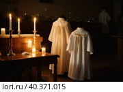 White robes for baptismal ritual in church by candlelight. Generative Ai. Стоковое AI-изображение, AI-художник Юрий Поздников / Фотобанк Лори