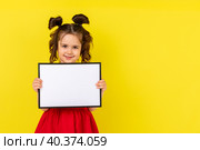 little brunette girl in red drees smiling and holding an empty drawing Board, space for text,isolate on a yellow background. Стоковое фото, фотограф Ирина Михайличенко / Фотобанк Лори