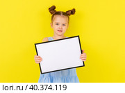 little blonde girl in blue drees smiling and holding an empty drawing Board, space for text,isolate on a yellow background. Стоковое фото, фотограф Ирина Михайличенко / Фотобанк Лори