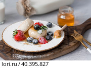 Cottage cheese pancakes, Russian cheesecakes with fresh blueberries, strawberries, honey and mint leaves on a stylish wooden board on a gray concrete table. Natural products. Healthy and delicious breakfast. Стоковое фото, фотограф Photojuli / Фотобанк Лори
