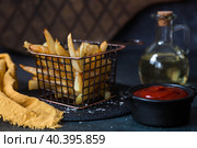 French fries in a metal basket with salt, ketchup and sunflower oil on a stylish board on a dark background. Fried potatoes. The concept of fast food and junk food. Стоковое фото, фотограф Photojuli / Фотобанк Лори
