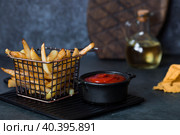 French fries in a metal basket with salt, ketchup and sunflower oil on a stylish board on a dark background. Fried potatoes. The concept of fast food and junk food. Стоковое фото, фотограф Photojuli / Фотобанк Лори