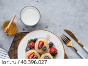 Cottage cheese pancakes, Russian cheesecakes with fresh blueberries, strawberries, honey and mint leaves on a stylish wooden board on a gray concrete table. Natural products. Healthy and delicious breakfast. Стоковое фото, фотограф Photojuli / Фотобанк Лори