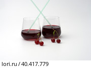 Two glasses of cherry straw drink on a white background. Next to them are paired cherry berries on peduncles. Copy space. Стоковое фото, фотограф Роман Дзюбало / Фотобанк Лори