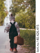 A little boy of 4 years old outdoors with a suitcase and a stuffed rabbit goes on a journey. A beautiful portrait of a child playing on the street. Стоковое фото, фотограф Photojuli / Фотобанк Лори