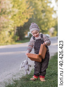 A little boy of 4 years old outdoors with a suitcase and a stuffed rabbit goes on a journey. A beautiful portrait of a child playing on the street. Стоковое фото, фотограф Photojuli / Фотобанк Лори
