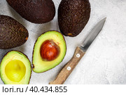 Whole and cut in half ripe organic avocados and a knife on a grey background. The Haas Avocado. Source of vitamins , trace elements , beta-carotene and omega-3 fatty acids . Healthy food, diet. Стоковое фото, фотограф Виктория Панченко / Фотобанк Лори