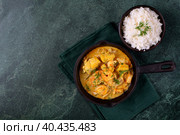 Fish curry with codfish, pollack and shrimps with coconut milk served in cast iron pan and bowl of rice on green table. Top view. Copy space. Стоковое фото, фотограф Оксана Чаюн / Фотобанк Лори