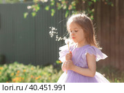 Happy beautiful girl blowing on a dandelion on a sunny summer evening. A child in the fresh air, in nature. The setting sun. Стоковое фото, фотограф Photojuli / Фотобанк Лори