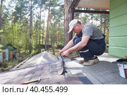 Male worker lays a sheet of soft flexible bitumen shingles on the roof of a country house. Стоковое фото, фотограф Кутина Татьяна / Фотобанк Лори