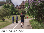 People walk in the park against the background of the palace of Tsar Alexei Mikhailovich in Kolomenskoye. A man does sports running in the park. Russia, Moscow, May 2023. Редакционное фото, фотограф Photojuli / Фотобанк Лори