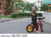 A cheerful little boy rides a bicycle outdoors. A happy child walks in the spring park. The kid is dressed in a fashionable sweater and denim overalls. Стоковое фото, фотограф Photojuli / Фотобанк Лори