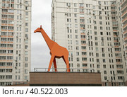 Город Москва, внутреннее пространство двора микрорайона "Новое Марфино". Каре "Жираф". Фигура оранжевого жирафа стоит на крыше подземного гаража на фоне жилого многоквартирного дома (2022 год). Стоковое фото, фотограф Наталья Николаева / Фотобанк Лори