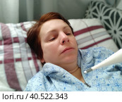 Sick woman in bed. Headache, runny nose and cold. Paleness of the face and faintness of the body. Feeling unwell. The patient lies on a pillow, holds a thermometer and measures the temperature. Стоковое фото, фотограф Юлия Петровская / Фотобанк Лори