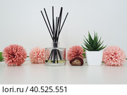 Composition of pink artificial flowers, incense sticks in a glass vase with essential oil. Still life on a white table. Aloe flower in a white pot. Room and apartment decor, interior design. Стоковое фото, фотограф Юлия Петровская / Фотобанк Лори